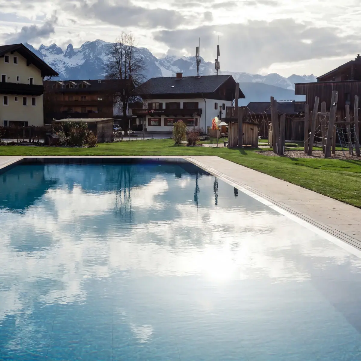 Ein Schwimmbecken in Werfenweng mit Gras und Gebäuden im Hintergrund.